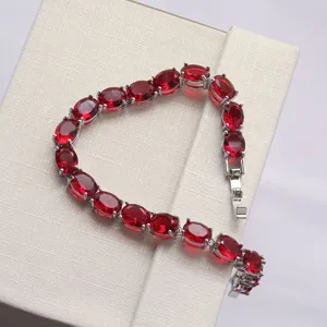 Nahaufnahme eines eleganten silbernen Armbands mit ovalen roten Edelsteinen auf einer Geschenkbox