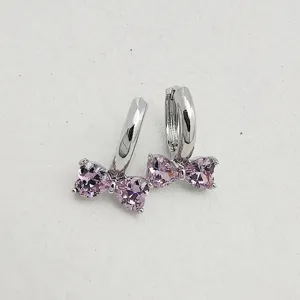 Close-up detail of silver huggie hoop earrings with pink heart zirconia bow.