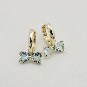 Detail shot of dainty bow hoop earrings featuring sparkling heart-shaped zircon stones in gold.