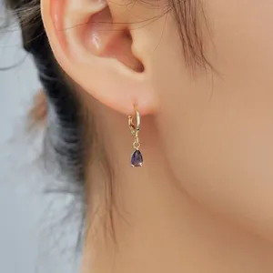 Primo piano dettagliato di eleganti orecchini dorati con una gemma viola brillante.
