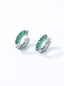 Primo piano di orecchini a cerchio argentati con zirconi color verde smeraldo.