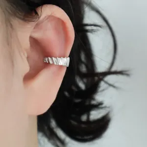 Close-up view of a minimalist silver geometric textured ear cuff on the ear.
