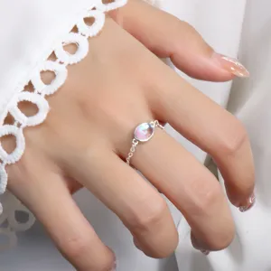 Detail shot of an elegant silver chain ring with an iridescent oval moonstone on the finger