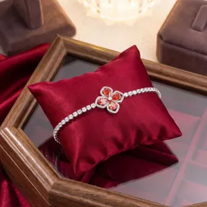 Detailed view of silver four-leaf clover bracelet with orange zircons on red satin pillow