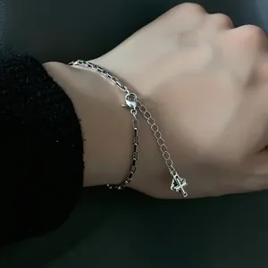Close-up shot of a minimalist silver chain bracelet with a cross and H letter charm