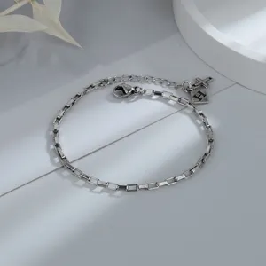 Detail of silver chain bracelet with cross and letter H charms in minimalist style