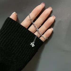 Macro view of a silver minimalist bracelet detailing the H-letter charm and cross pendant.