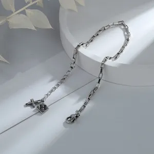 Macro detail of silver box chain bracelet featuring a cross charm and H letter tag