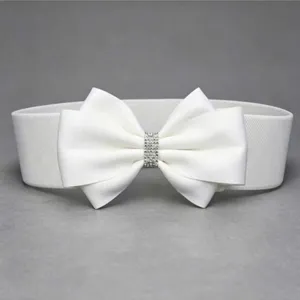 Close-up detail of white elastic waist belt featuring a rhinestone bow decoration.