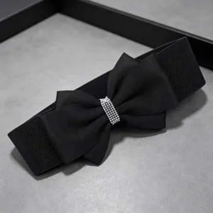 Detail view of a black wide elastic waist belt featuring a chic fabric bow and rhinestone buckle.