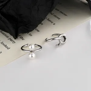 Primer plano de ear cuffs plateados con nudo y perla sobre un fondo de página de libro.