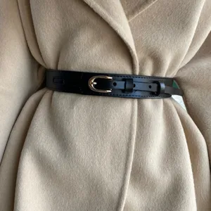 Stylish black PU leather waist belt with gold pin buckle detail worn over beige coat.