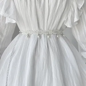Detailed macro shot of an elegant bohemian white pearl waist chain on a dress.