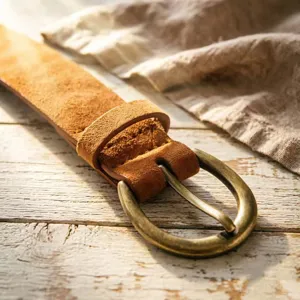 Close-up detail of the vintage caramel suede belt with antique brass buckle and wood background.