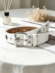 Detail shot of white punk leather belt with silver metal grommets and classic buckle on table.