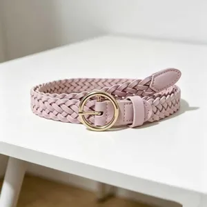 Close-up of pink braided leather belt with gold round buckle, minimalist women style.