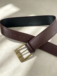 Dettaglio in primo piano della cintura in pelle marrone scuro con fibbia in ottone e cuciture.