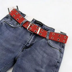 Gros plan sur une ceinture en toile rouge à double œillets sur un jean bleu, boucle argent.