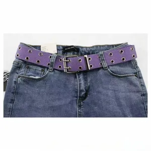 Vue détaillée d'une ceinture en toile violette à double œillet portée sur un jean bleu