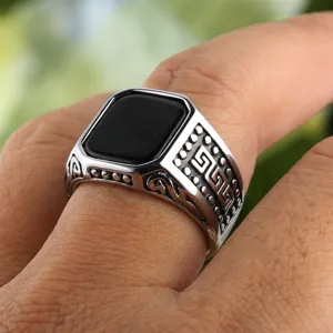 Close-up van heren zegelring van titanium staal met zwarte onyx steen en Grieks sleutelpatroon