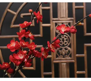 Detail shot of artificial red plum blossoms with traditional Chinese wooden screen background.