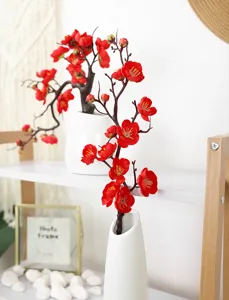 Close-up of lifelike artificial red plum blossoms displayed in a minimalist white ceramic vase