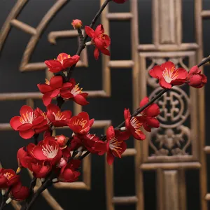 Vivid red artificial plum blossoms with realistic details against a Chinese screen background.
