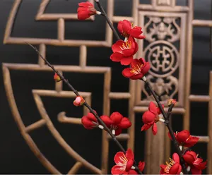 Close-up view of artificial red plum blossom branches with realistic silk petals and natural stems.