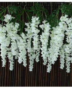 Macro view of realistic artificial white wisteria hanging flowers and lush green leaves