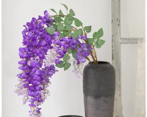 Macro view of purple artificial wisteria flowers in a dark ceramic vase for decor.