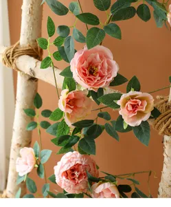 Vista detallada de enredadera de peonía artificial rosa con hojas sobre madera de abedul