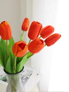 Close-up view of artificial orange tulips bouquet in clear glass vase, home table decor.