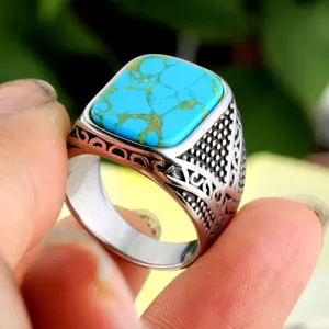 Detailweergave van een vierkante turquoise steen in een gegraveerde roestvrijstalen ring.