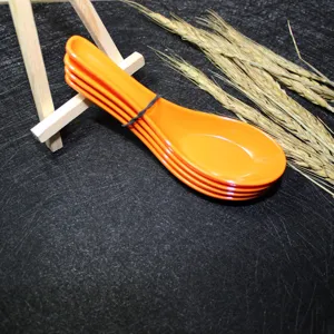 Close-up of four orange melamine soup spoons stacked on a black textured background