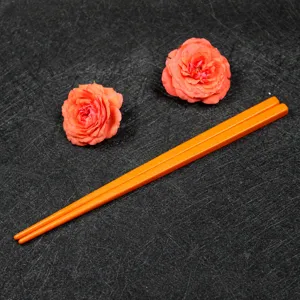 Close-up of bright orange melamine chopsticks for kids with flower props on black background