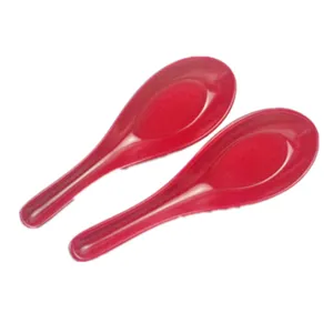 Macro detail of two glossy red melamine Chinese soup spoons on a plain white background