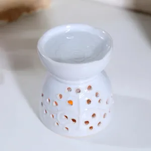 White ceramic oil burner and wax melt warmer with delicate cut-out tree pattern for home decor.