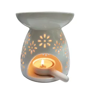 Ceramic oil burner with hollow floral pattern and candle spoon for home fragrance and decor.
