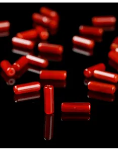 Macro detail of natural red agate tube beads scattered on reflective black surface