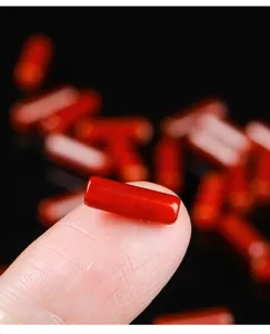 Detailed macro view of a polished natural red agate cylinder bead on a fingertip