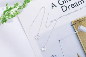 Detail view of silver ginkgo leaf threader earrings with fine chain on artistic background.