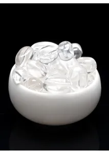 Primer plano de cuentas de cristal de roca natural de alta claridad en un bol de cerámica blanca.