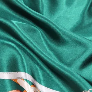 Gros plan sur la texture satinée d'un foulard en soie vert avec des motifs de chaîne.