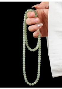 Detailed macro view of 108 natural pale green Hetian jade mala beads held in hand.