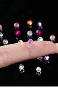 Makro-Detail von 4 mm schillernden Kristallglasperlen auf einem Finger als Maßstab
