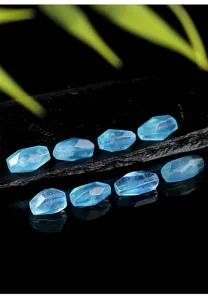 Detalle de cuentas de aguamarina natural talladas sobre una superficie negra reflectante