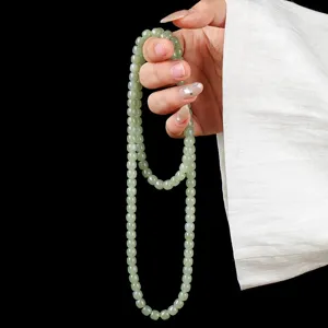 Natural light green Hetian jade 108 prayer beads held against a dark black background