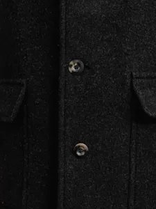 Detailaufnahme der dunklen Wollstofftextur und der Schildpattknöpfe an einem Herrenmantel