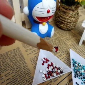 Close-up of white wax dotting pencil picking up red rhinestones for DIY crafts