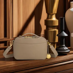 Elegant vintage-style beige leather camera bag with gold hardware displayed on wooden furniture
